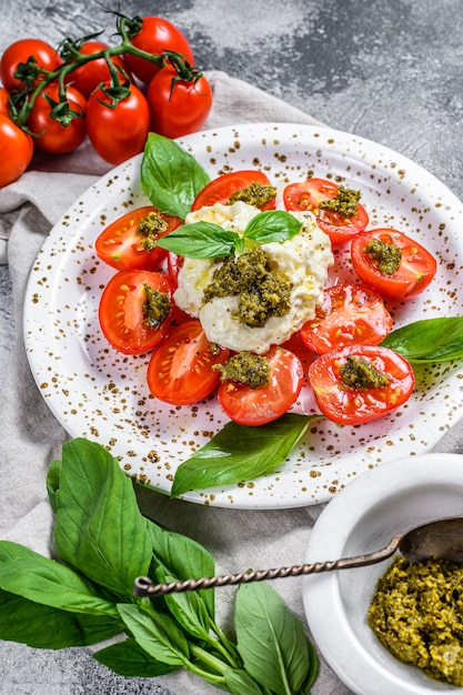 Stracciatella au fromage italien (mozzarella buffalo) sur une petite assiette servie avec des tomates fraîches et du basilic.