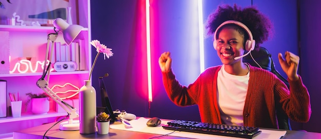 Une streameuse afro-américaine jouant aux combats en ligne avec une équipe qualifiée d'Esport portant des écouteurs dans une salle d'éclairage aux couleurs néon Parler à d'autres joueurs en planifiant des stratégies pour gagner des concurrents Tastemaker