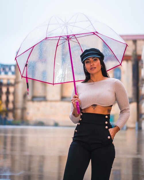 Street Style d'une jeune brune sous la pluie de la ville avec un parapluie