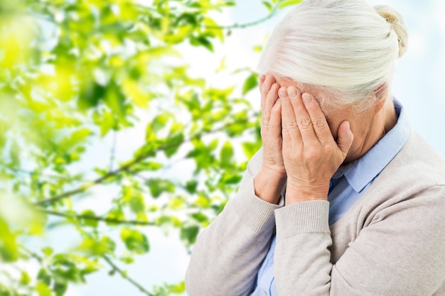 stress, âge et concept de personnes - femme âgée souffrant de maux de tête ou de chagrin sur un fond naturel vert