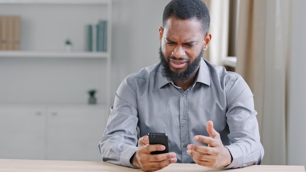 Stressé déçu afro-américain ethnique barbu avec téléphone portable lisant de mauvaises nouvelles Employé de bureau homme d'affaires avec smartphone triste avec échec erreur d'application de paiement en ligne problème de service cellulaire