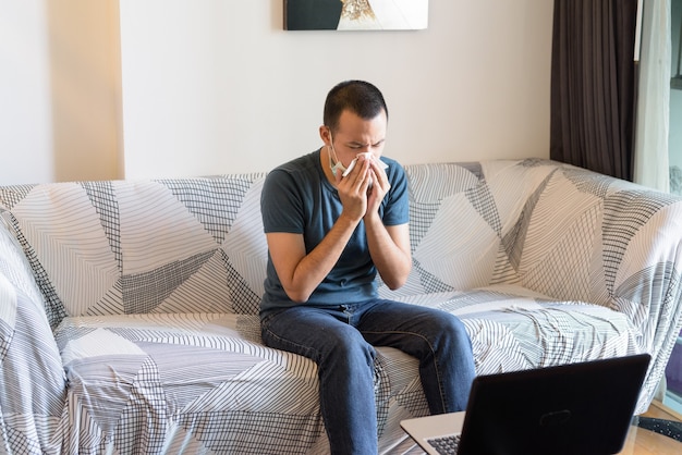 Stressé jeune homme asiatique avec masque tomber malade et se moucher à la maison en quarantaine