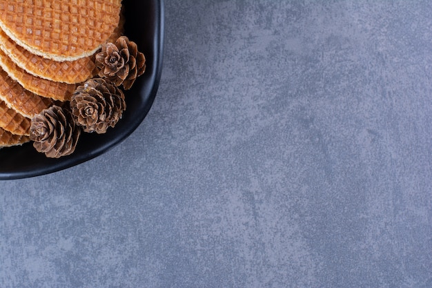 Stroopwafels aux pommes de pin isolé dans une plaque noire sur une surface en pierre