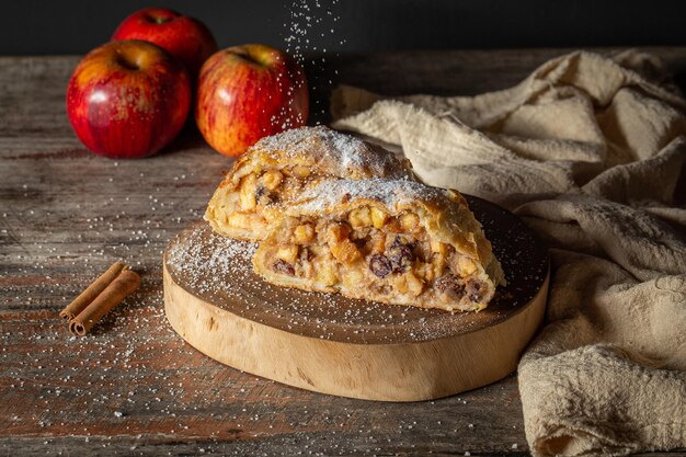 Strudel aux pommes à la cannelle et aux raisins secs sur fond rustique saupoudrant de sucre en poudre sur le dessus