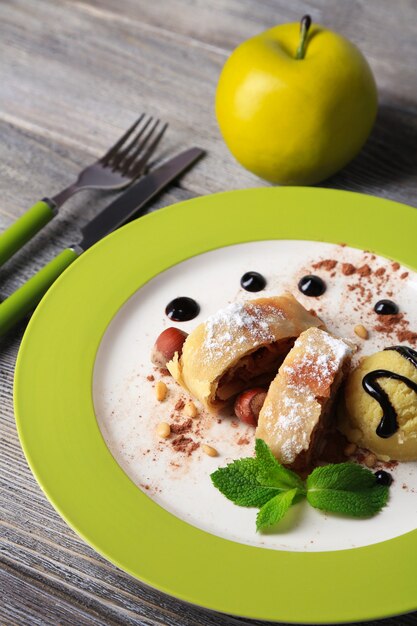 Strudel aux pommes maison savoureux avec noix, feuilles de menthe et glace sur assiette, sur fond de bois