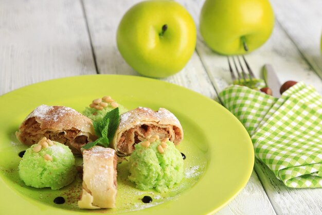 Strudel aux pommes maison savoureux avec noix, feuilles de menthe et glace sur assiette, sur fond de bois