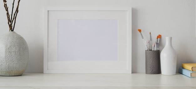 Studio d'artiste minimal avec cadre photo vide et fournitures de bureau sur un bureau blanc et un mur blanc