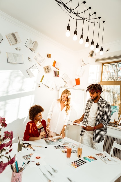 Studio décoré. Trois jeunes artistes se sentant joyeux et excités tout en travaillant dans un studio décoré de lumière