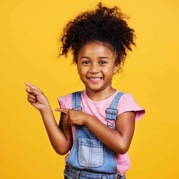 Studio de portrait et enfant heureux pointant la main vers l'espace avec un sourire sur le visage sur fond jaune Jeune fille enfant avec bonheur attitude insouciante et positive pour montrer l'accord de maquette de placement de produit