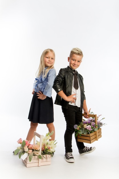 Studio portrait garçon et fille habillé en uniforme scolaire avec des compositions florales de voeux dans des paniers en bois, concept de félicitations, fond blanc, espace de copie