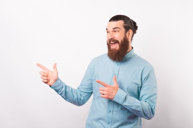 Stupéfait homme barbu hurlant en désinvolture pointant vers le mur blanc