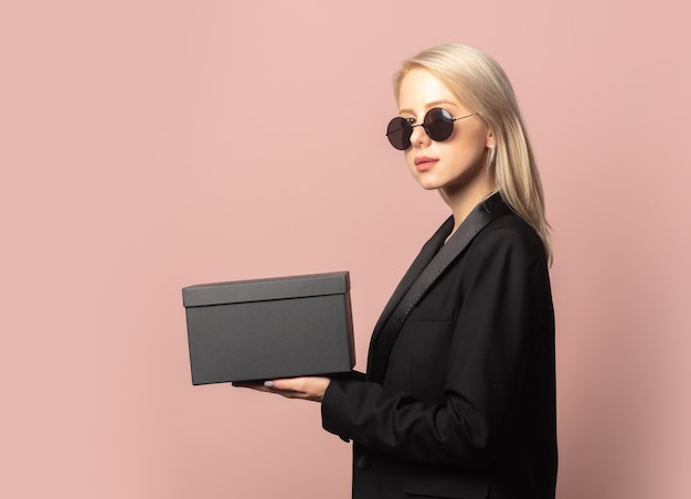 Style blonde en blazer et lunettes de soleil avec boîte-cadeau noire sur rose