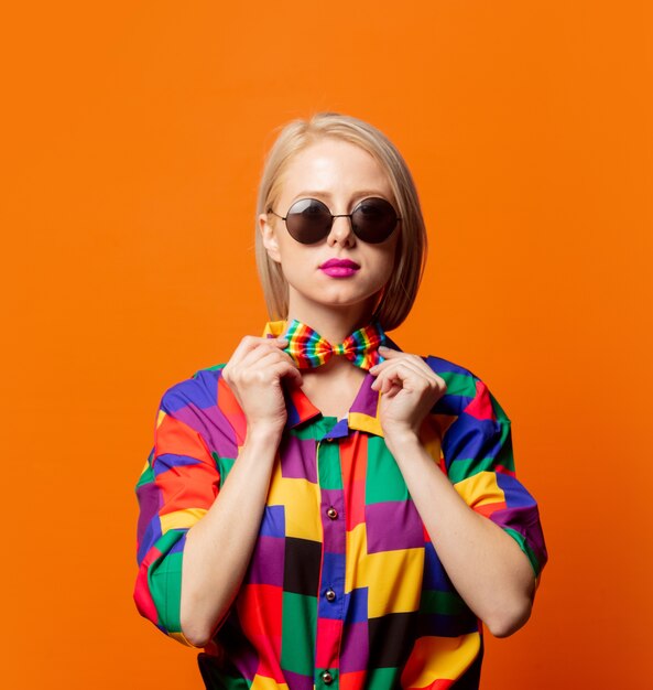 Style blonde dans des vêtements des années 90 avec un nœud papillon LGBT sur orange