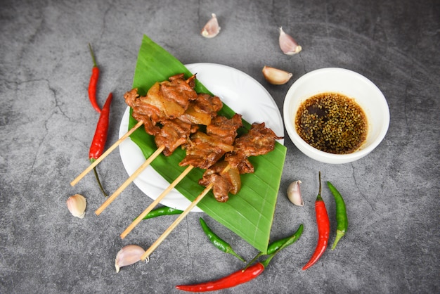 Style de la cuisine de rue asiatique thaïlandaise de porc grillé, tranches de bâtonnets de brochette de porc grillées sur une feuille de bananier sur une assiette blanche avec sauce au piment ail