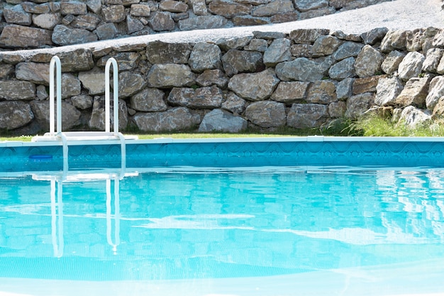 Style de détente luxueux. Vue sur la piscine turquoise avec pelouse verte et un mur en pierres. Vacances concept, aménagement paysager, parc aquatique, hôtel