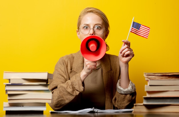 Style femme blonde en assis à table avec le drapeau américain et mégaphone avec des livres autour de jaune