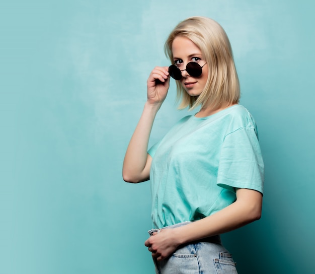 Style femme blonde à lunettes de soleil sur le mur bleu