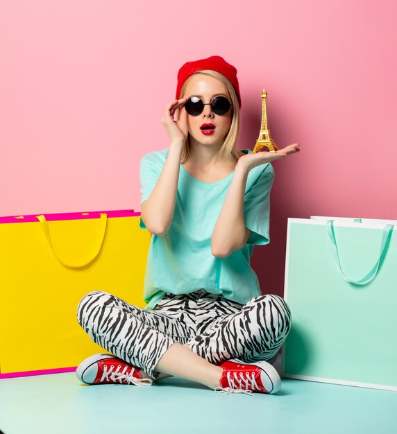 Style femme à lunettes de soleil avec des sacs à provisions et petite tour Eiffel sur mur rose