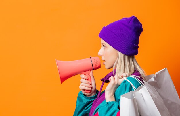 Style femme en survêtement des années 90 avec mégaphone et sacs à provisions sur orange