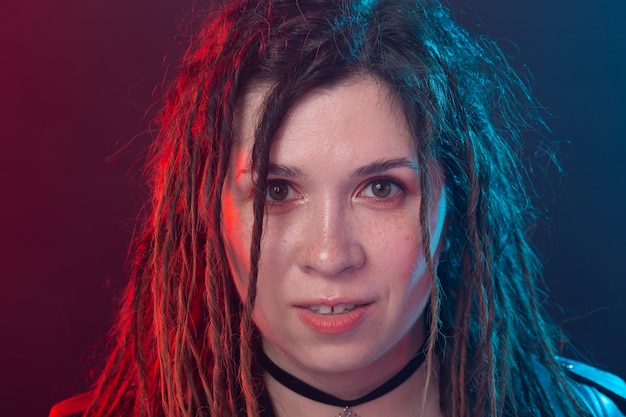 Style, jeunesse, concept de personnes - jeune femme joyeuse avec dreadlock ressemble à un rocker sur sombre