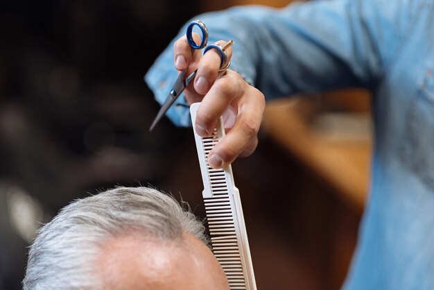 Style professionnel. Gros plan du coiffeur masculin peignant les cheveux des personnes âgées avant de commencer à le coiffer.