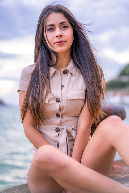 Style de rue, une jolie jeune brunette caucasienne assise avec une salopette courte brune en été au bord de la mer