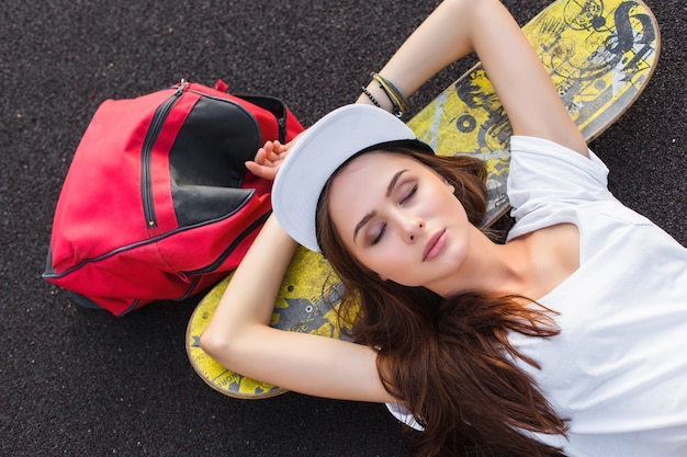 Photo style urbain de belle femme rue posant en plein air sur l'aire de jeu avec skateboard et sac à dos de voyage