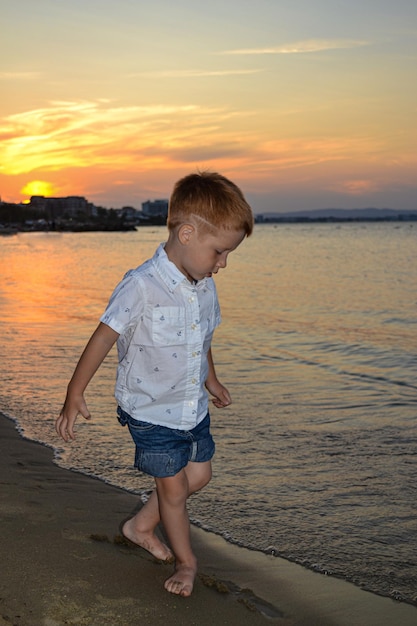 Style de vie enfance heureuse enfant rousse petit garçon marchant sur la plage au bord de la mer au coucher du soleil belle côte en Bulgarie
