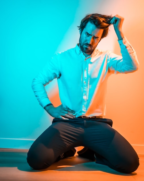 Style de vie en studio, look doux d'un homme de race blanche dans une chemise blanche, éclairé par une lumière au néon orange et bleu