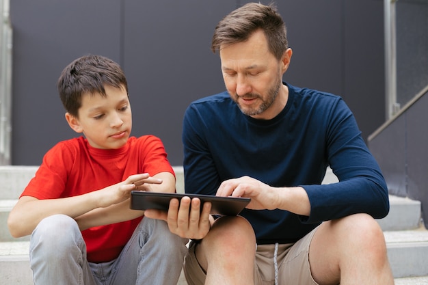 Le style de vie urbaine de la famille moderne. Papa et fils utilisent une tablette sur les marches d'un escalier en béton. Concept de technologie moderne