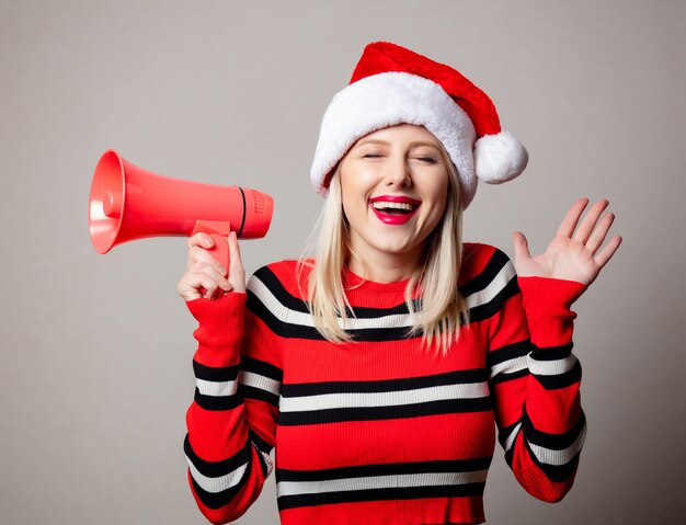 Styled woman in Christmas hat avec mégaphone sur mur gris