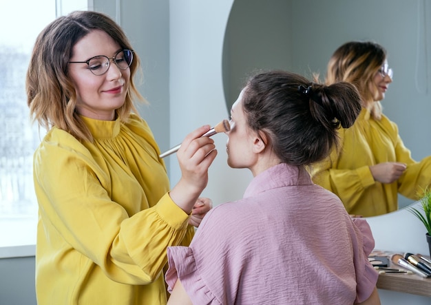 Styliste de beauté appliquant le maquillage à un jeune mannequin Maquilleur professionnel faisant du glamour