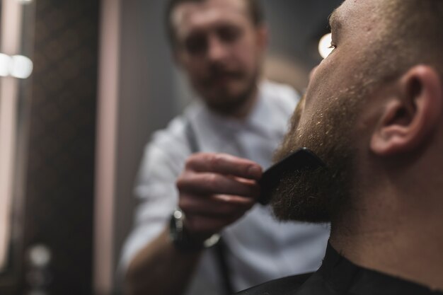 Styliste floue peignant la barbe du client