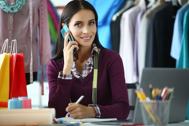 Styliste de jeune femme parlant au téléphone sur le lieu de travail dans l'atelier. Acceptation des commandes pour le concept de personnalisation