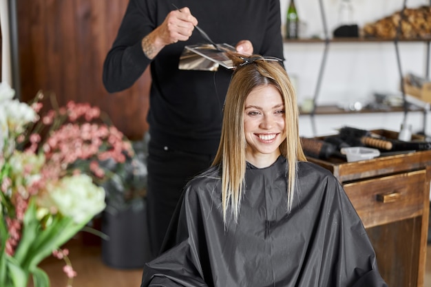 Le styliste masculin confiant est la teinture des cheveux d'une cliente blonde caucasienne