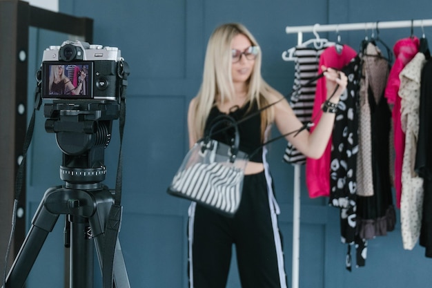 Styliste de mode vlogging influenceur des médias sociaux créant du contenu vidéo en streaming femme montrant un sac debout dans la salle d'exposition de vêtements