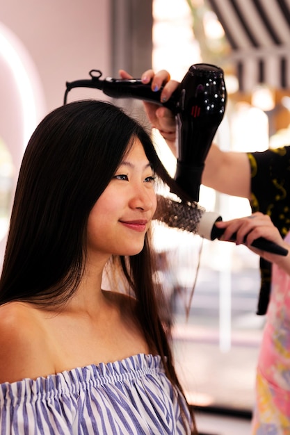 Styliste peignant les cheveux de la femme avec une brosse et un sèche-cheveux