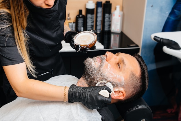 Styliste professionnel dans un salon de coiffure élégant et moderne rase et coupe les cheveux d'un jeune homme