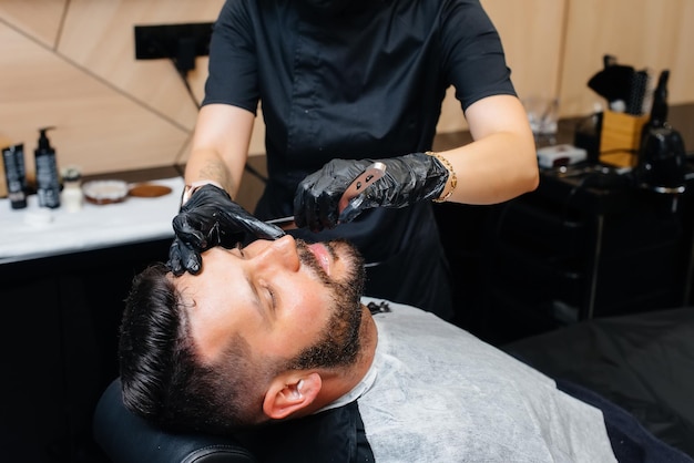 Un styliste professionnel dans un salon de coiffure moderne et élégant rase et coupe les cheveux d'un jeune homme. Salon de beauté, salon de coiffure.