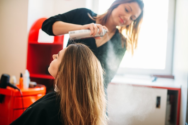 Le styliste se prépare à appliquer de la mousse, une coiffure féminine dans un salon de coiffure. Fabrication de coiffure dans un salon de beauté