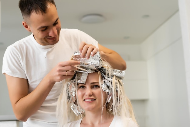 Un styliste souriant est en train de mourir les cheveux longs, le coiffeur homme teint les cheveux d'une femme