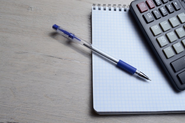 Un stylo à bille et une micro-calculatrice reposent sur un cahier carré. fermer.