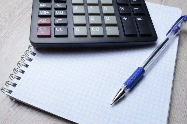 un stylo à bille et une micro-calculatrice reposent sur un cahier carré. fermer.