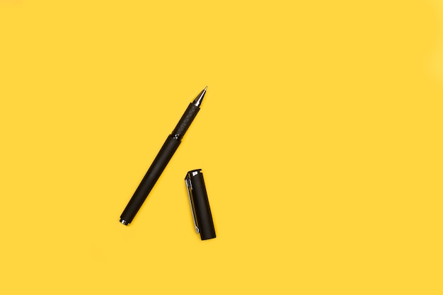 Un stylo à bille noir ouvert sur fond jaune avec espace copie