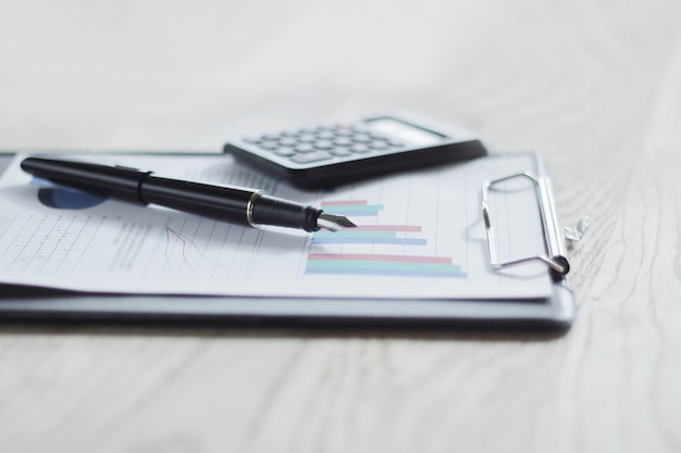 stylo, calculatrice et presse-papiers sur table en bois.