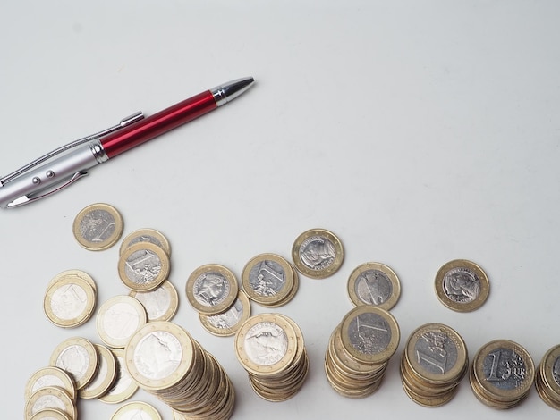 Un stylo est à côté d'une pile de pièces en euros.