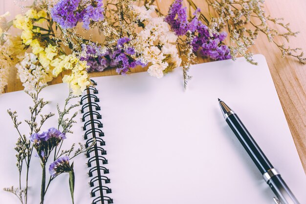 Stylo mis sur un cahier vierge près de bouquet de fleurs, sur une table en bois