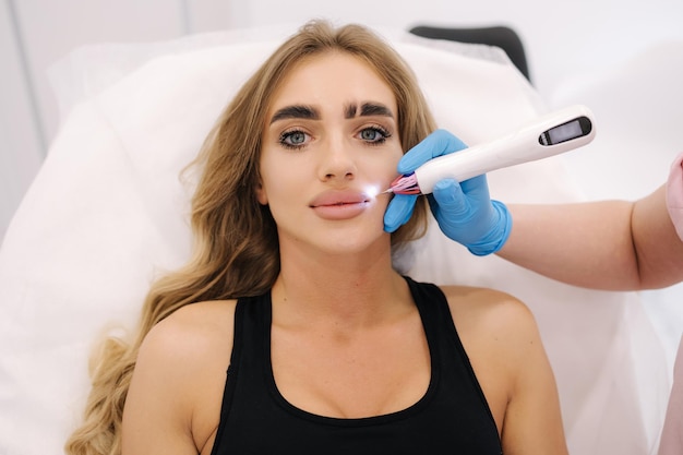 Stylo plasma réduisant les rides autour de la joue sur la jeune femme vue de dessus pf femme à la clinique de cosmétologie