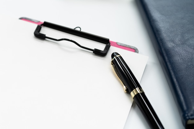 Stylo et presse-papiers avec une feuille blanche, lunettes sur livre de journal sur fond blanc