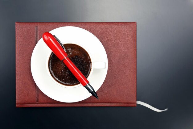 Le stylo rouge est sur la tasse avec du café noir et un cahier